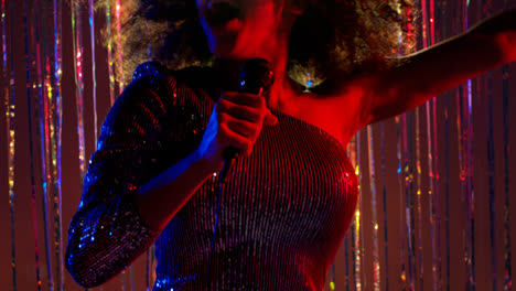 Young-Woman-With-Microphone-Singing-At-Karaoke-Nightclub-Bar-Or-Disco-With-Sparkling-Lights-In-Background-4